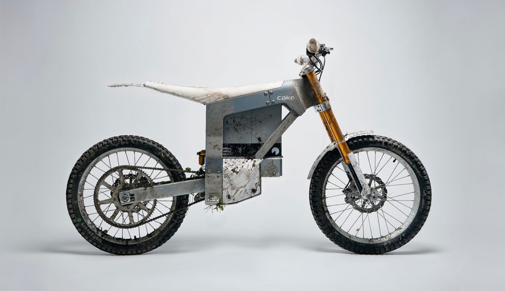 A cake electric dirt bike in a photo studio covered in mud and grass