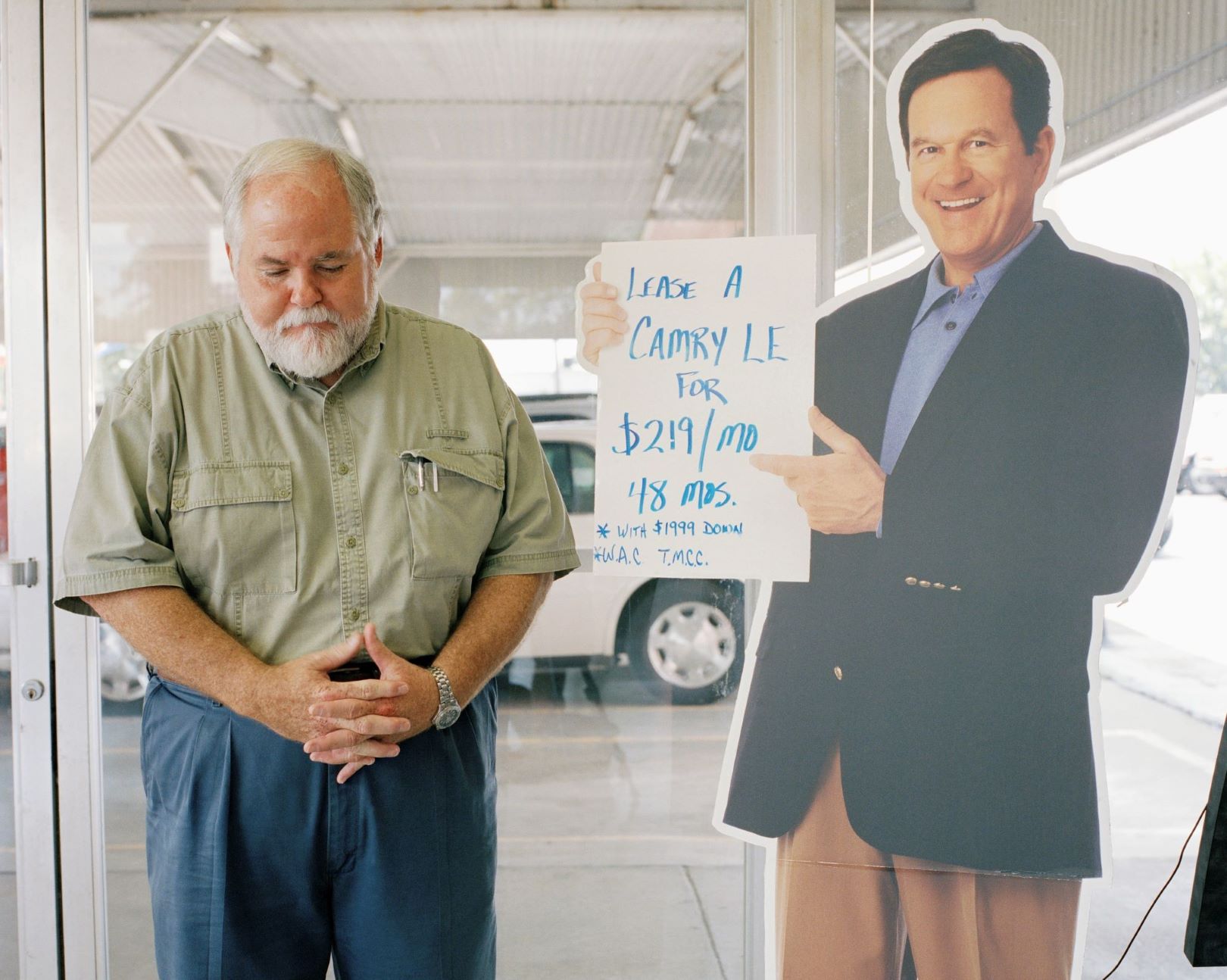 Car salesperson standing next to a cardboard cutout of another car salesperson