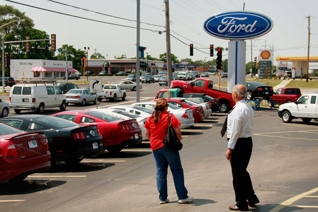 Car salesperson standing next to a customer at a Ford dealership