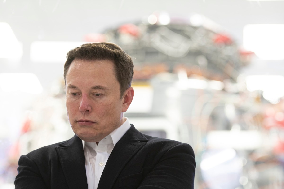 Tesla Motors CEO Elon Musk photographed wearing a black blazer with white button up shirt looking down towards his right. Photo shot at Musk's SpaceX facility
