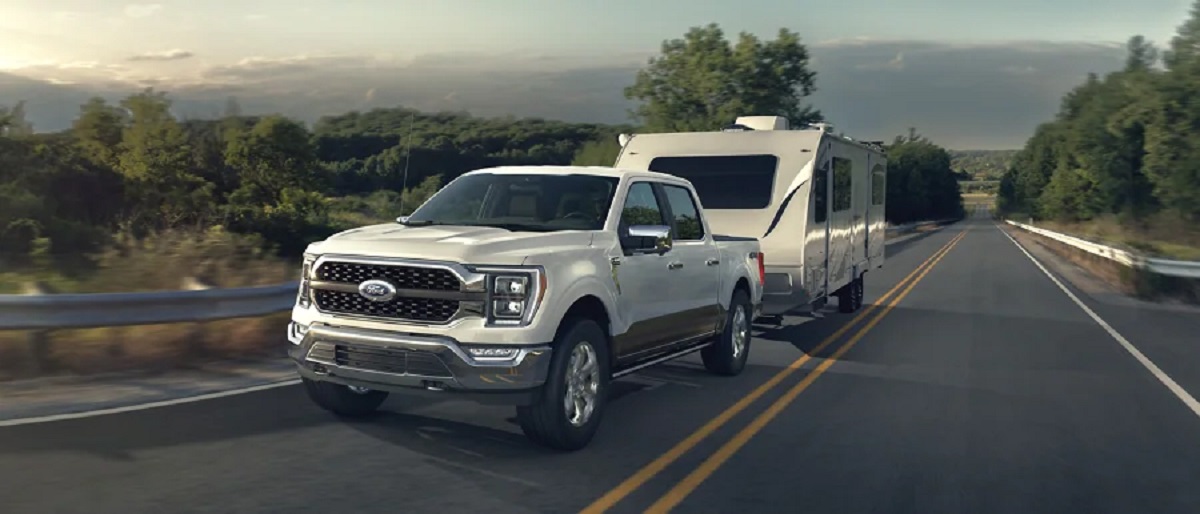 A white 2021 Ford F-150 pulling a trailer on the highway.