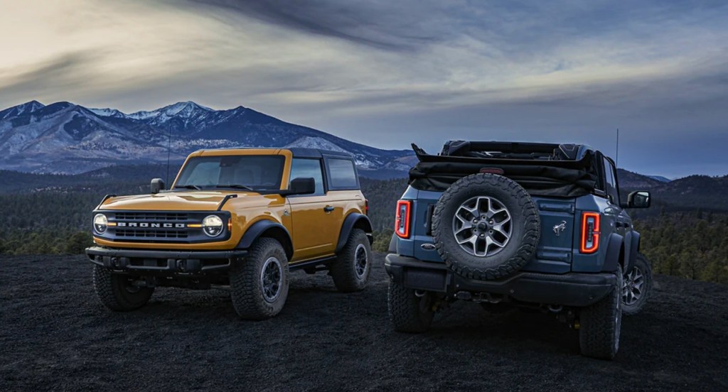 A yellow and a blue Ford Bronco are parked off-road. 