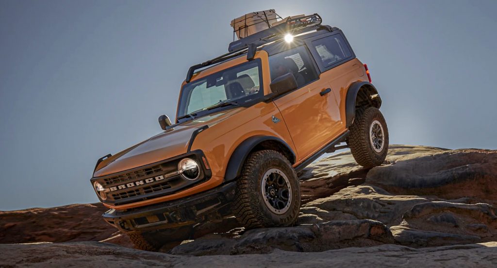 A yellow Ford Bronco is driving on rocks.