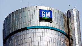 A silver building with a blue ring around the top in the shape of circle and the GM logo at the top. GM feels the microchip shortage.