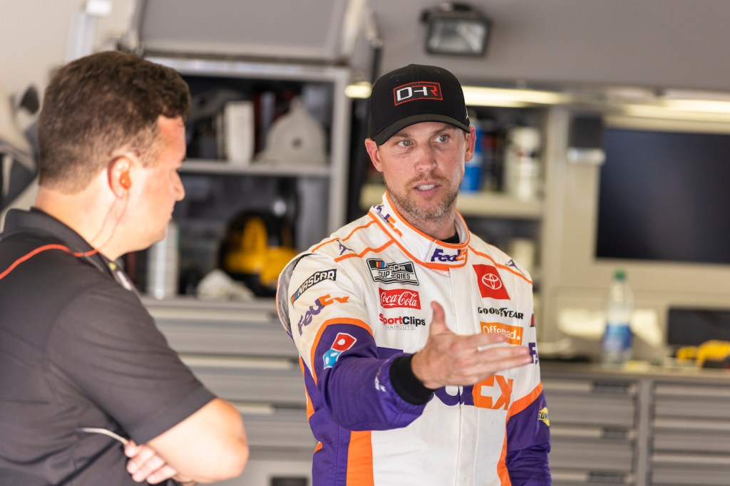 Denny Hamlin, Driver of the #11 NASCAR Next Gen car, talks with a team member in the garage during the NASCAR Cup Series test at Daytona International Speedway. After a NASCAR Next Gen crash test went poorly, Hamlin demanded information from officials. | James Gilbert/Getty Images