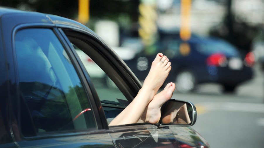 This is a photo of a woman sticking her bare feet out of the passenger window of a car. There are multiple ways to get in legal trouble while driving naked. | Essdras M Suarez/ Globe Staff/ MET/Getty Images