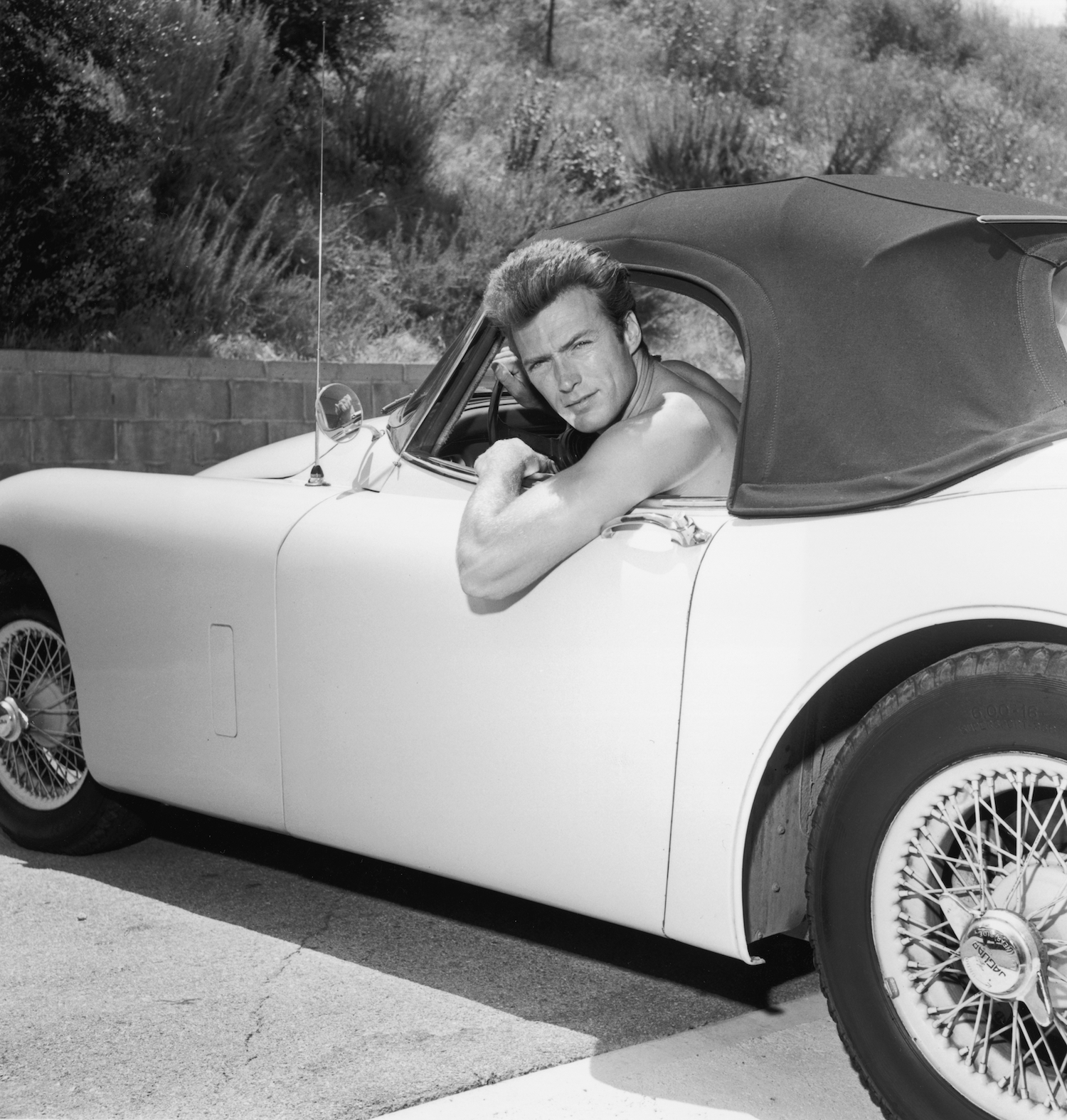 Clint Eastwood poses shirtless in his Jaguar convertible. Traffic laws do not dictate drivers' outfits. Penal laws do. Driving shirtless is not illegal wherever being shirtless in public is legal. Drivers are not exempt from public decency and indecent exposure laws.  | Hulton Archive/Getty Images