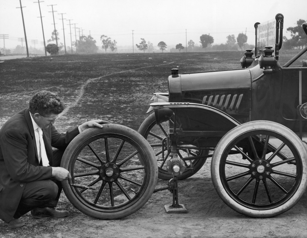 A man kneels outdoors to change the front tire on his Model 'T' Ford in 1915. He is demonstrating one of the first models with replaceable tires. Slow leaks have always been an annoying problem, but you can use soap to find a slow tire leak or valve stem leak. | Camerique Archive/Getty Images