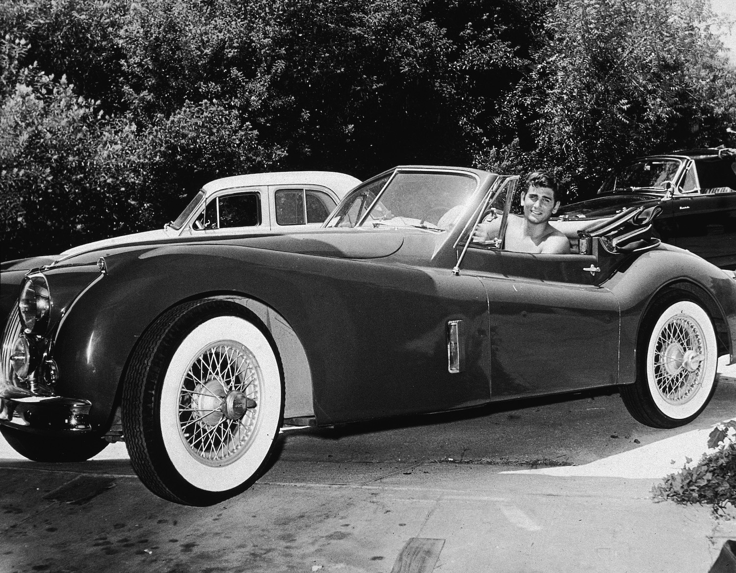Actor Michael Landon shirtless in his Jaguar XK140. Traffic laws do not dictate drivers' outfits. Traffic laws do not dictate drivers' outfits. Penal laws do. Driving shirtless is not illegal wherever being shirtless in public is legal. Drivers are not exempt from public decency and indecent exposure laws.| Hulton Archive/Getty Images
