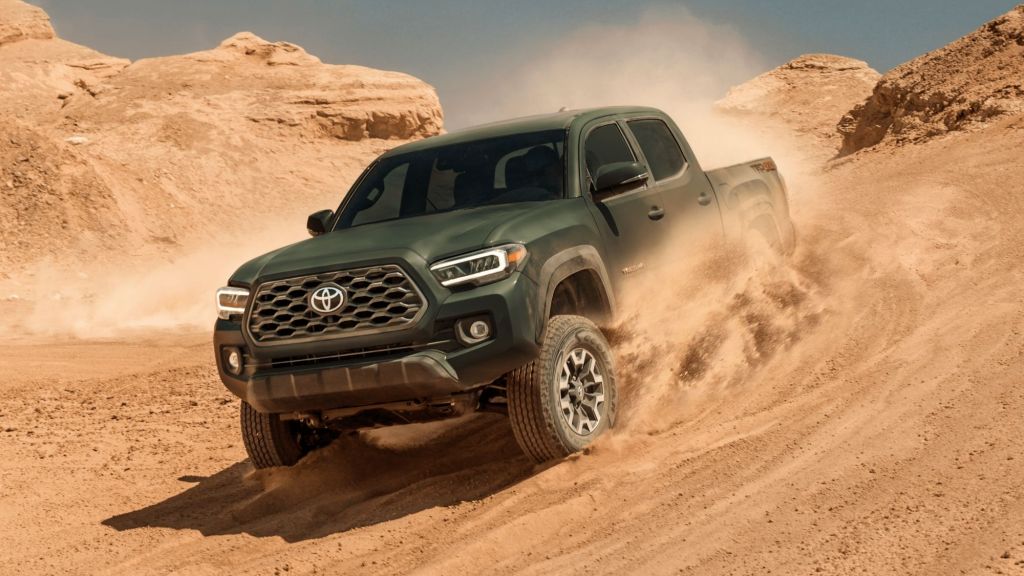 A green 2022 Toyota Tacoma driving down a sandy hill. 