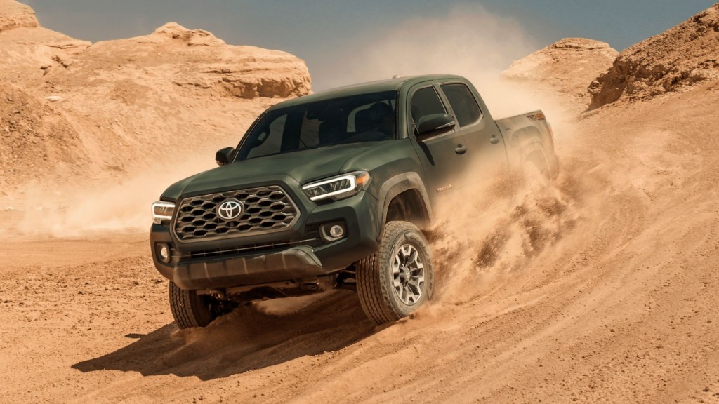 A green 2022 Toyota Tacoma driving down a sandy hill. 