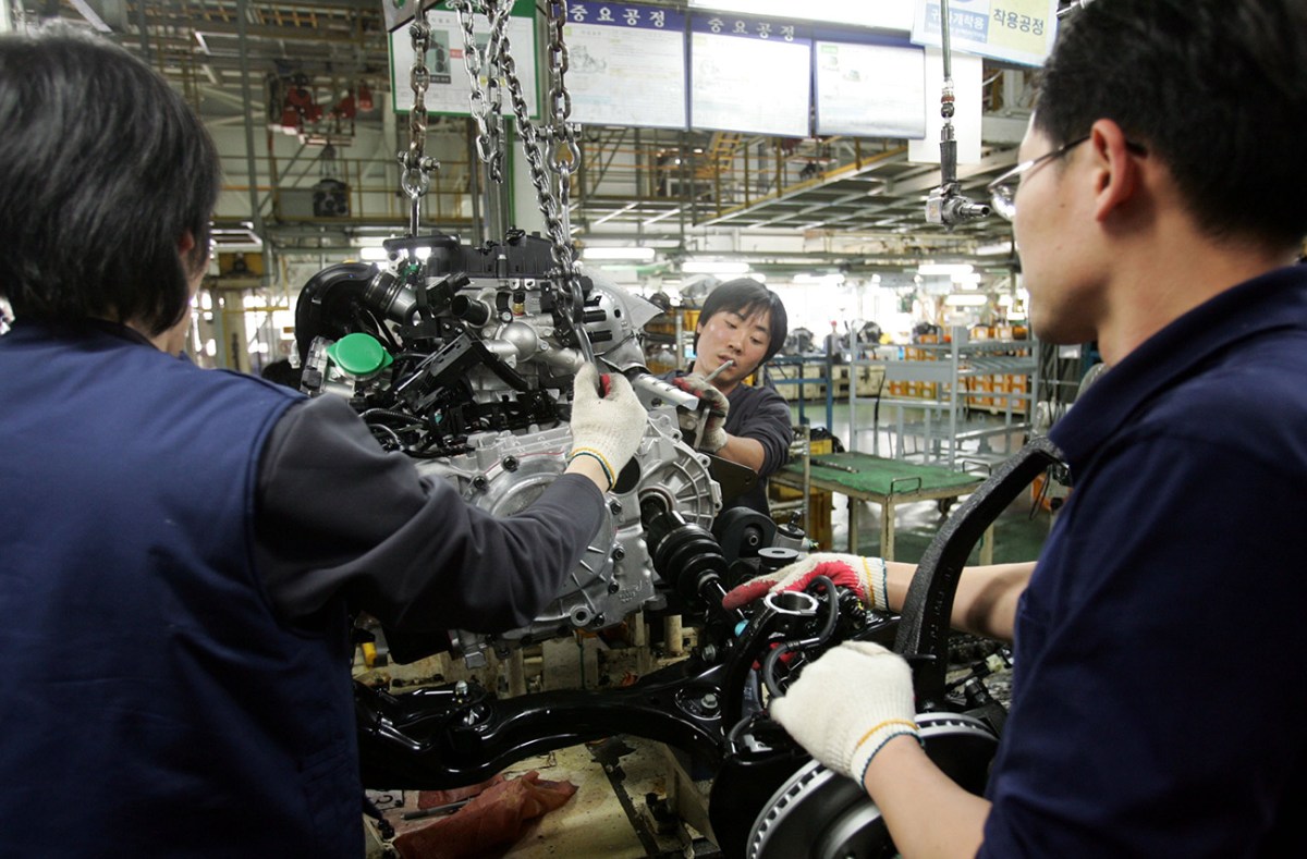 A Hyundai assembly plant with several auto workers installing an engine