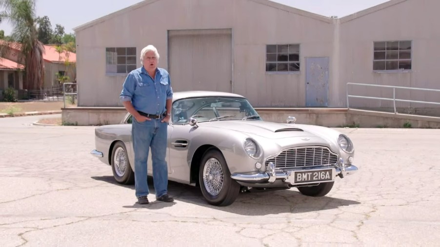 Jay Leno with a silver 1964 Aston Martin DB5 Goldfinger Continuation in a parking lot