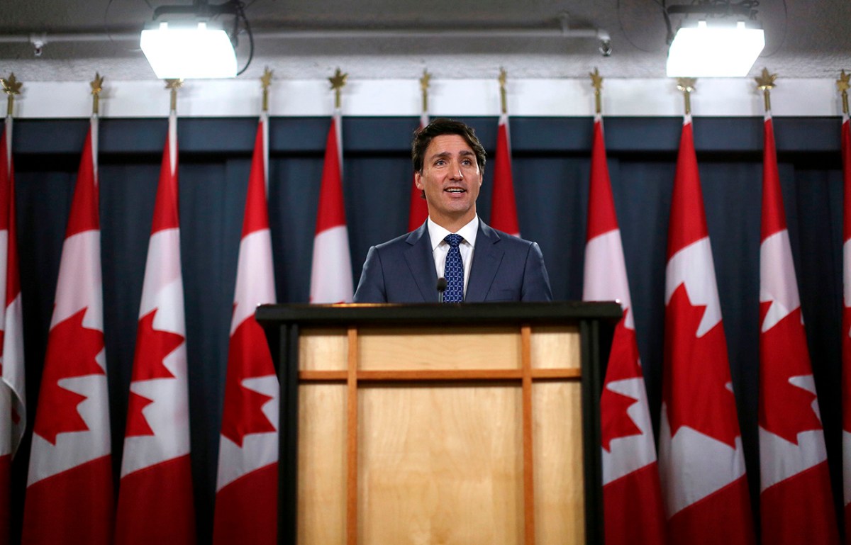 Canadian Prime Minister Justin Trudeau at a podium with a row of Canadian flags behind him. Recently members of the Canadian Parliament spoke out about the new U.S. EV tax credits bill as a possible negative for the Canadian auto industry 
