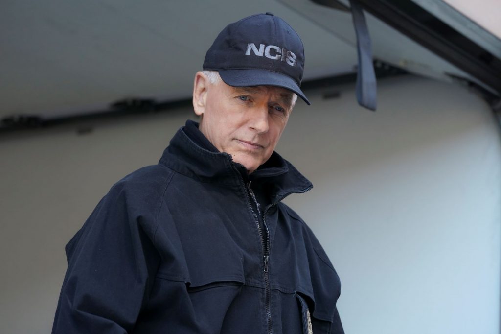 Mark Harmon from NCIS wearing a black hat and black jacket in a white room.