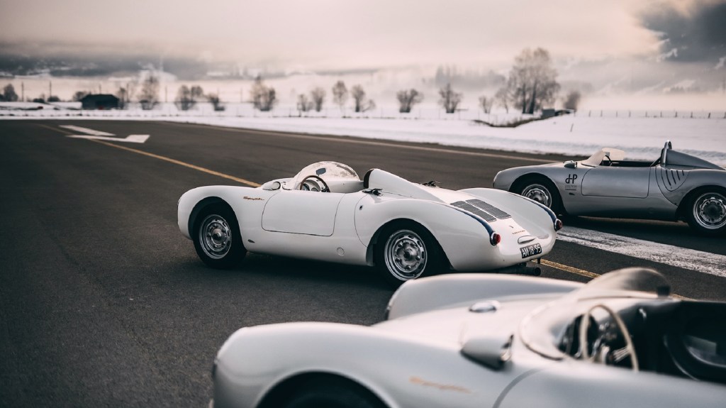 The rear side 3/4 view of several white and silver Porsche 550 Spyders on an Austrian runway