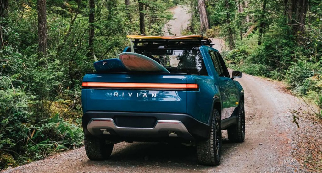 A blue 2022 Rivian R1T electric truck is driving on a dirt road. 