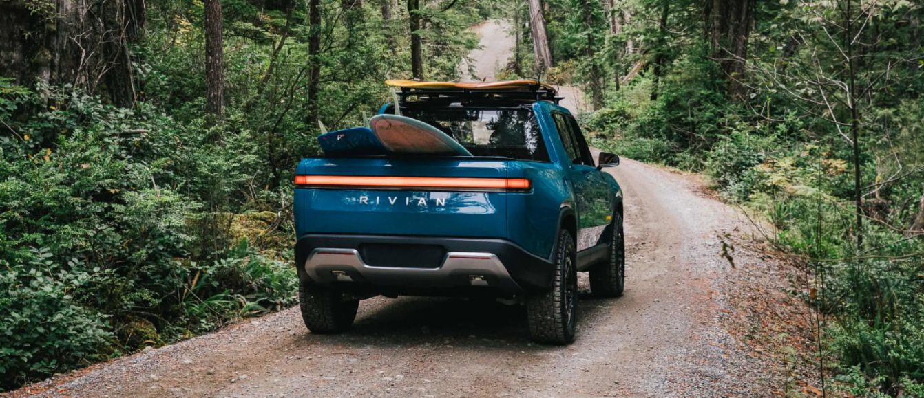 The Rivian R1T electric truck in blue driving on a forest trail