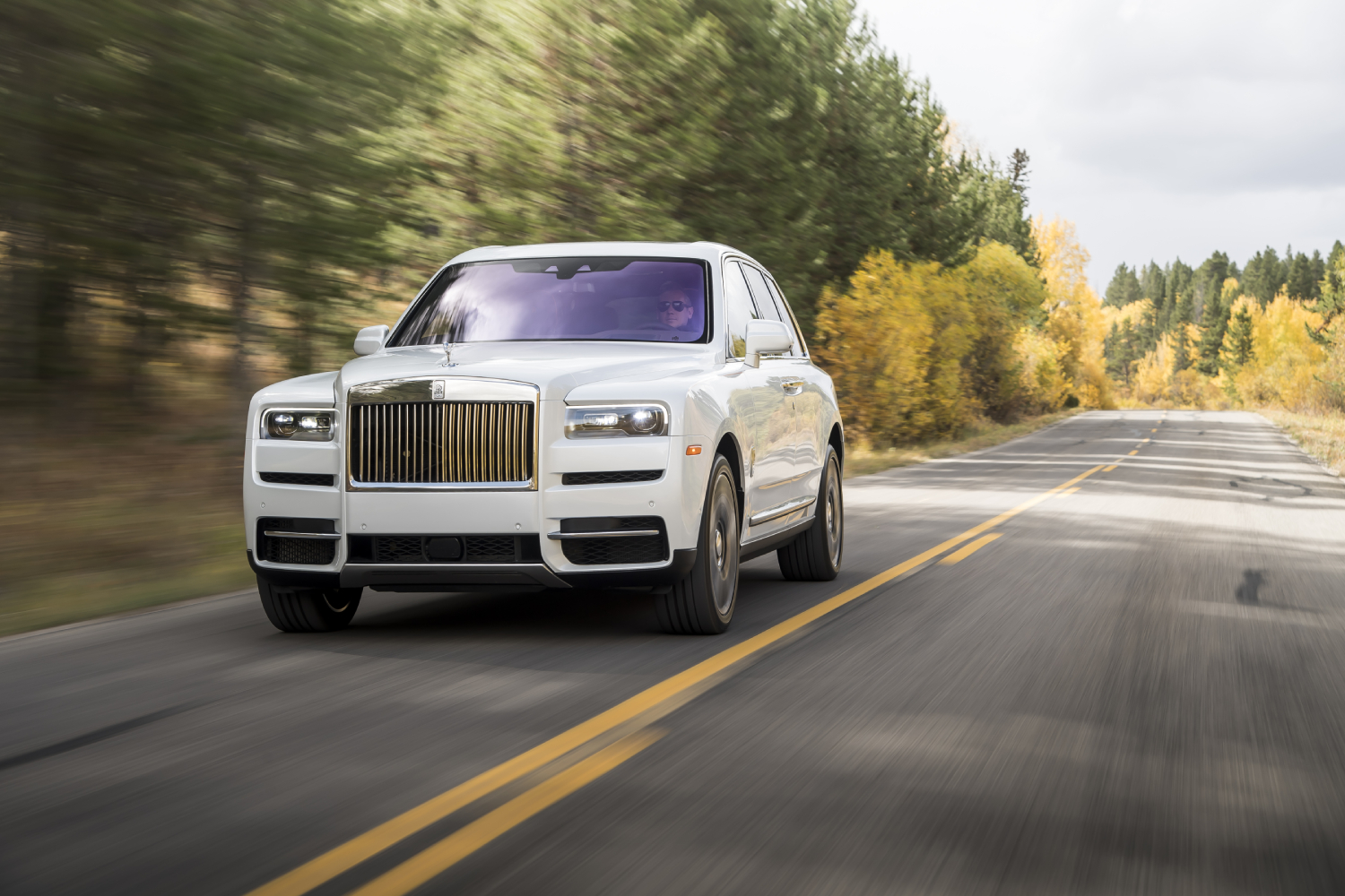 A white Rolls-Royce Cullinan driving down the road. This one is similar to the Cullinan recently added to Rick Ross' massive car collection.