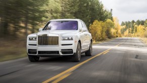 A white Rolls-Royce Cullinan driving down the road. This one is similar to the Cullinan recently added to Rick Ross' massive car collection.