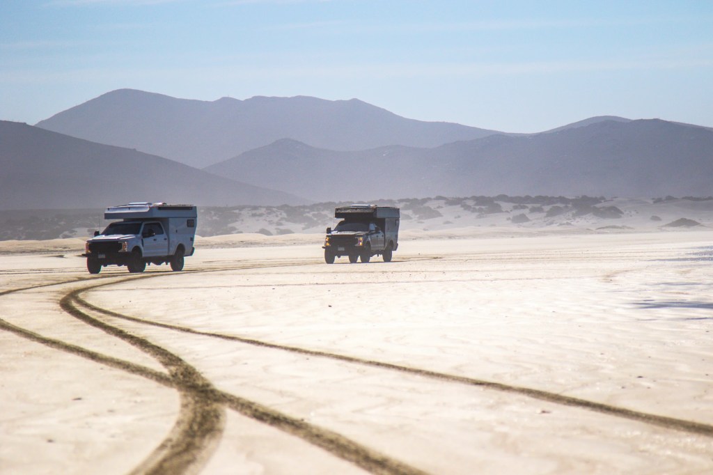 Two camper trucks driving through the desert 
