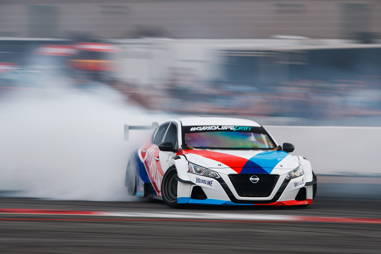 A 2021 widebody Nissan Altima shot while drifting as a large billowing cloud of tire smoke trails the vehicle. This car will be on display at SEMA 2021