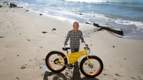 Yellow SONDORS electric bike on a beach with a man holding it up.