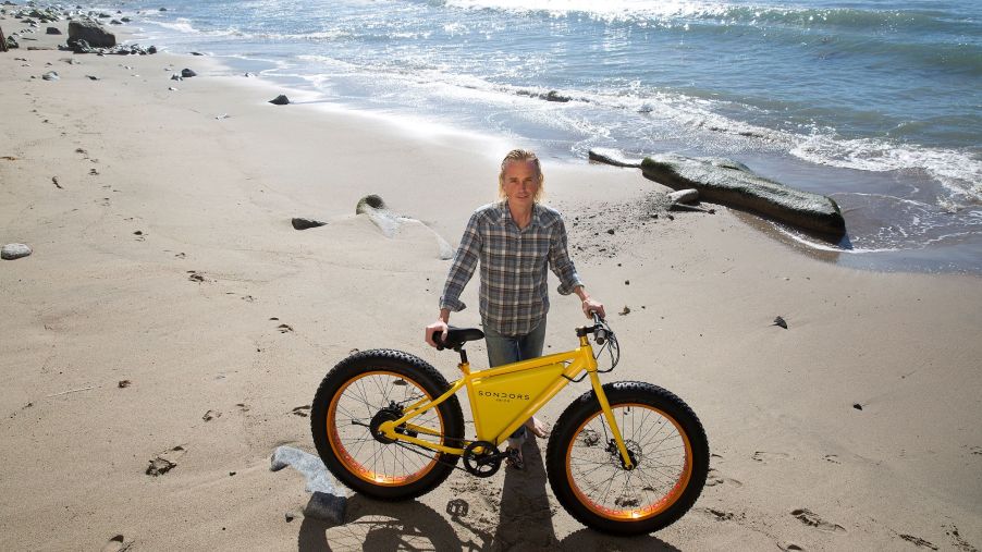Yellow SONDORS electric bike on a beach with a man holding it up.
