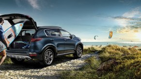 A blue 2022 Kia Sportage parked in front of the ocean. A man loads a surfboard into the back of the car.