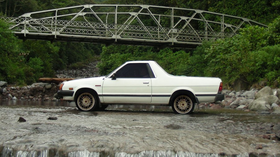 A white Subaru Brat parked near a bridge