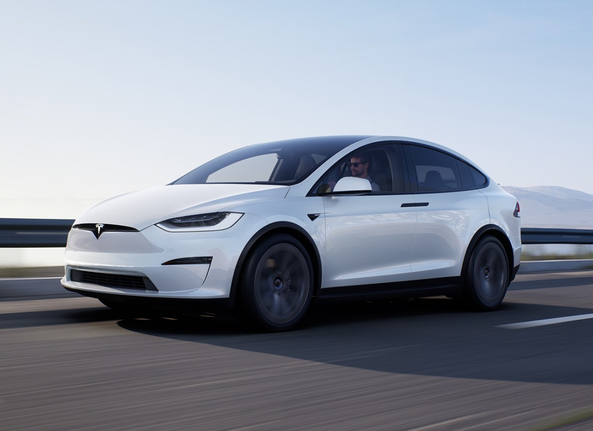 A white Tesla Model X driving on a road with the ocean in the background.