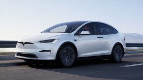A white Tesla Model X driving on a road with the ocean in the background.