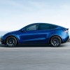 Tesla Model Y in blue shot from the side as it drives long a road. The Model Y is part of a recent Tesla suspension recall