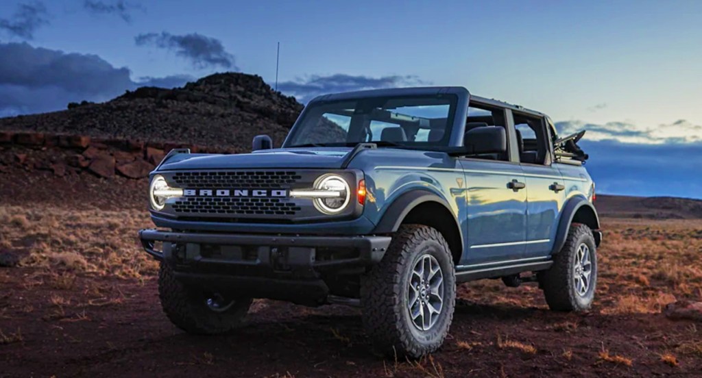 A blue 2021 Ford Bronco is parked outdoors with its headlights on. 