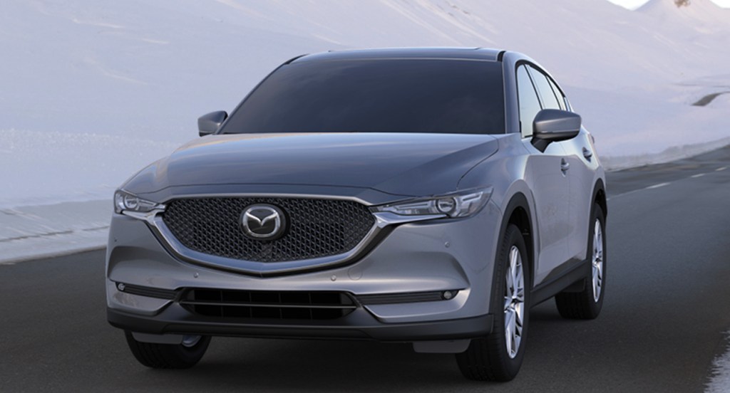 A gray Mazda CX-5 is driving on the road through a snowy area.