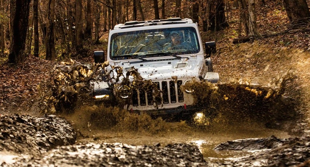 A gray Jeep Wrangler 4xe is driving through a pit of mud.