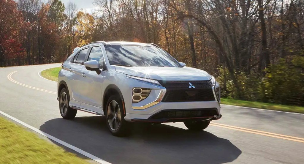 A white Mitsubishi Eclipse cross is driving down the road. 