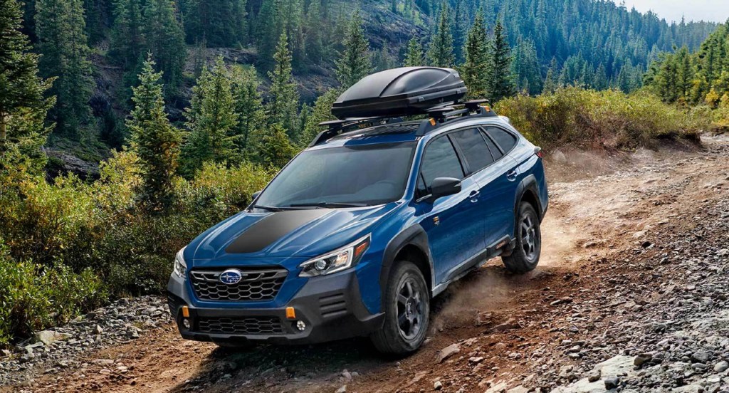 A blue Subaru Forester Wilderness drives through the forest on a dirt road.