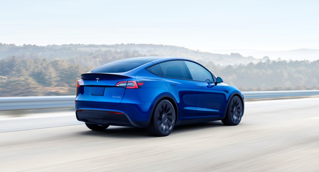 A blue Tesla Model Y electric crossover vehicle is driving on the road. 