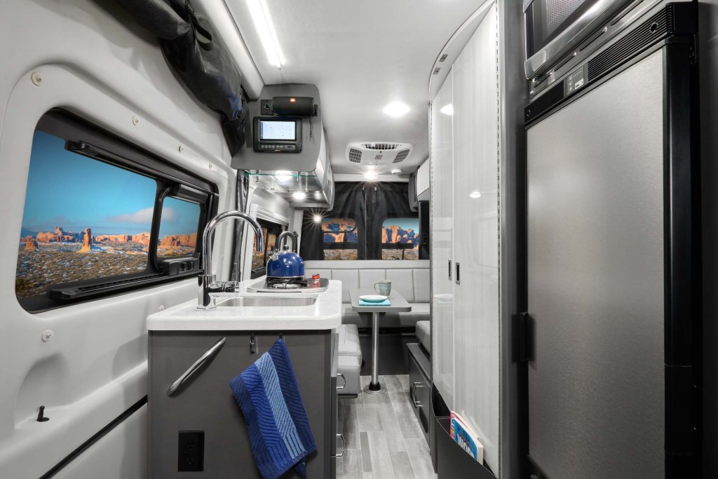 The silver-and-white kitchen, bathroom, and sleeping area of a Thor Motor Coach Tranquility 19P