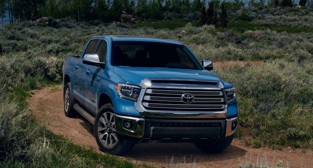 A blue Toyota Tundra is driving on a dirt road in nature. 
