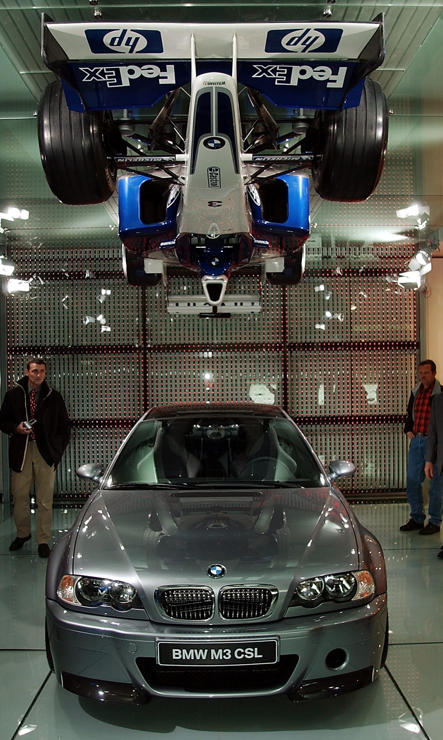A BMW M3 CSL sits beneath a Williams/BMW Formula 1 car suspended from the ceiling