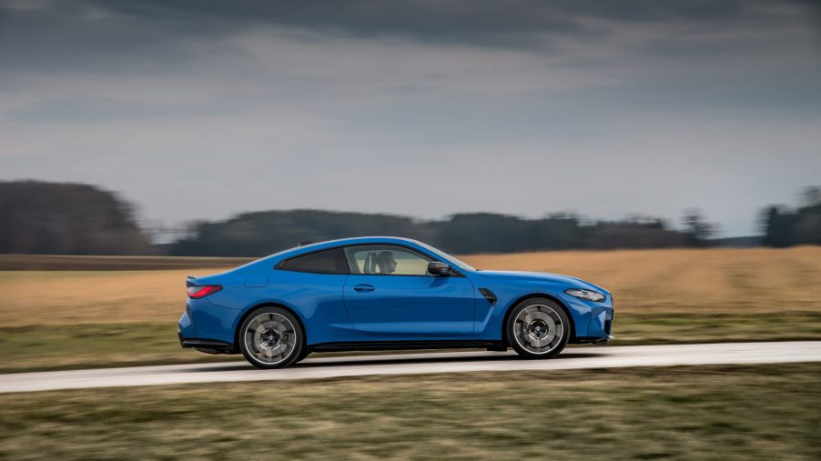 A blue BMW M4 shot in profile on a forested road