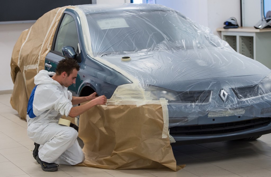 A young apprentice puts protections onto a car as he prepares to paint a car.
