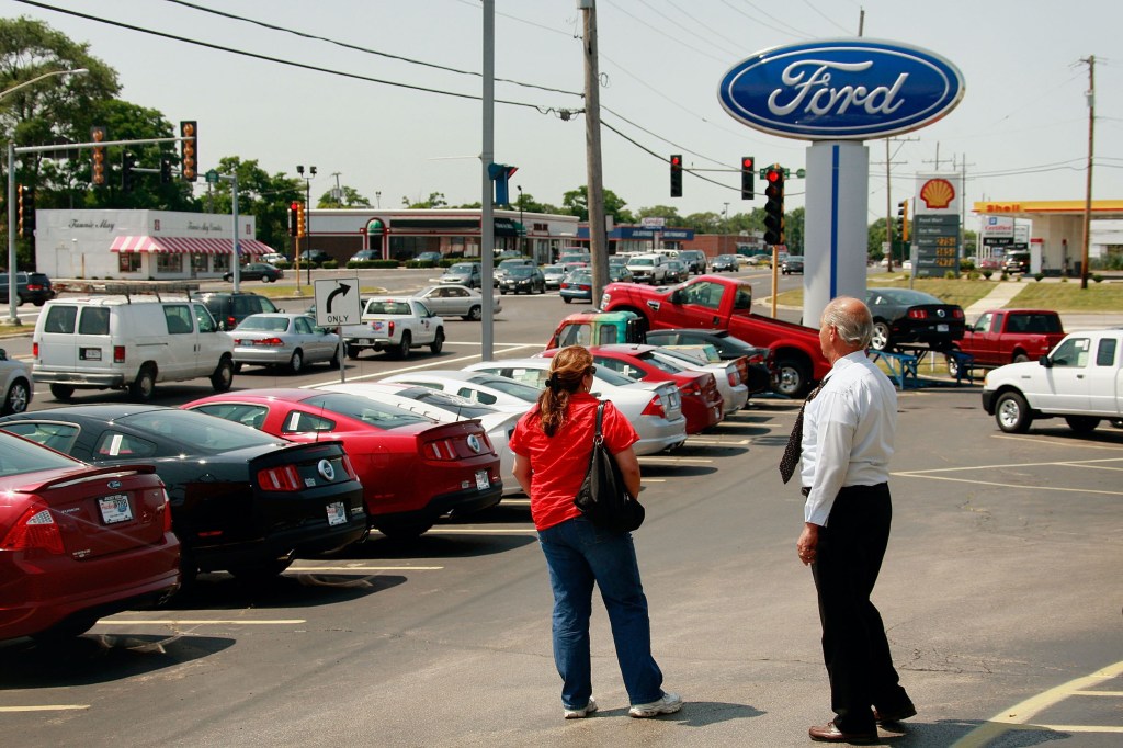 A car salesperson and a customer on a Ford dealer car lot. 