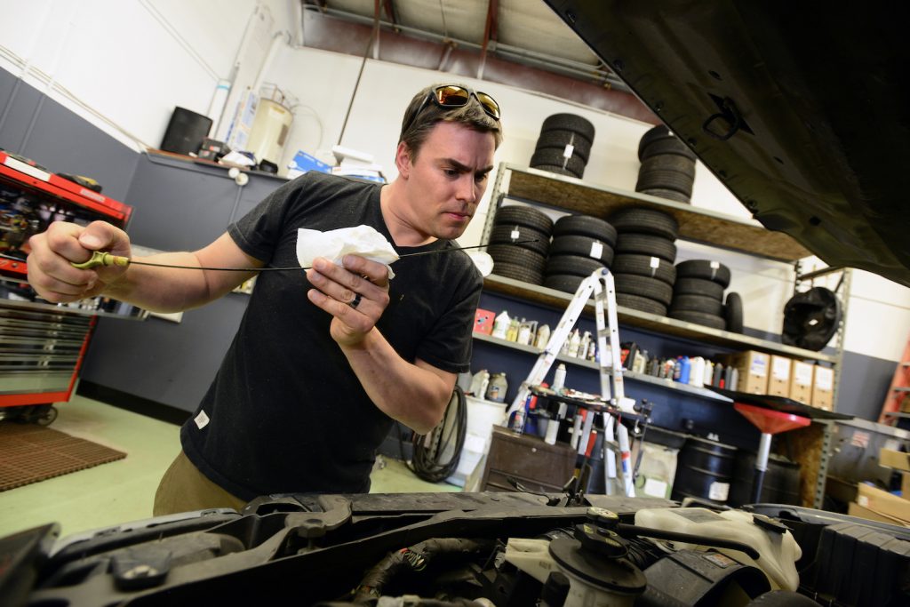 A mechanic checks a car's oil on a car. 