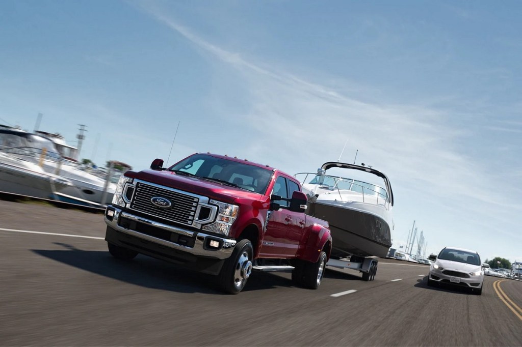 A red 2021 Ford F-450 towing a boat down the highway.