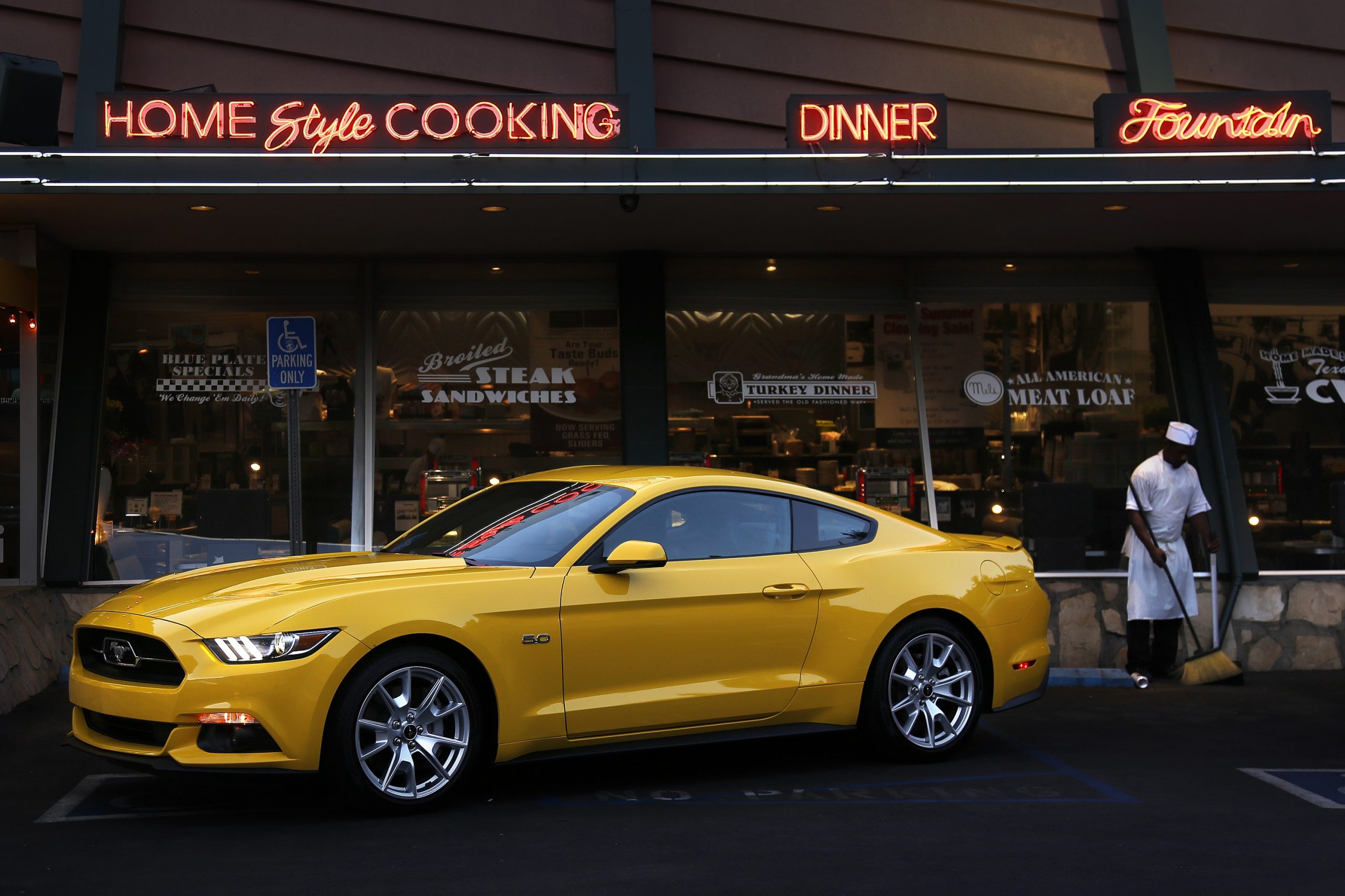 A yellow Ford Mustang sits outside a cafe, shot from the front 3/4 angle