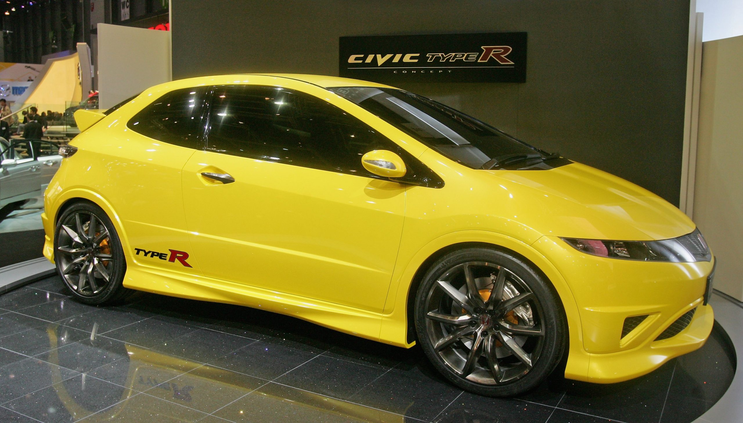 A yellow Honda Civic Type R on display at an auto show, shot in profile