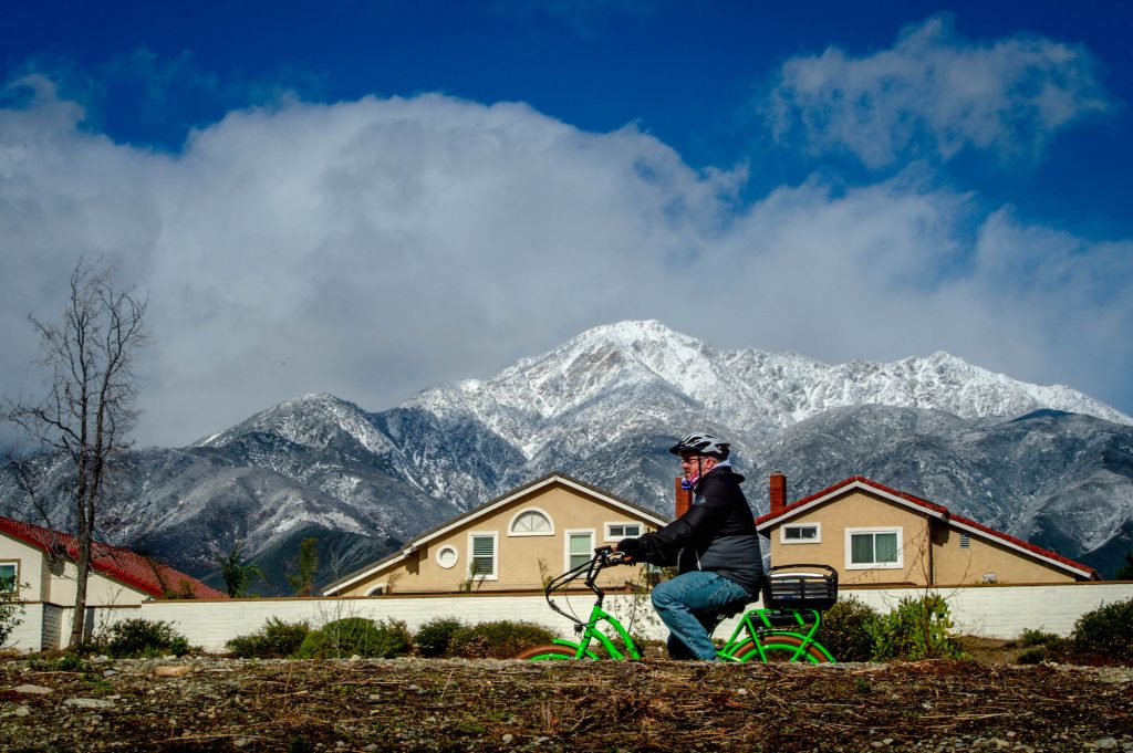 A cyclist rides a bike along the Pacific Electric Trail in Rancho Cucamonga against a backdrop of the snow-capped San Gabriel Mountains.